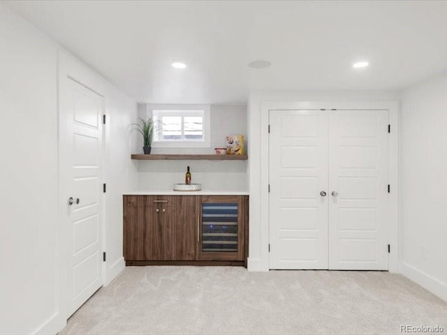 bar featuring beverage cooler, light colored carpet, a bar, and baseboards