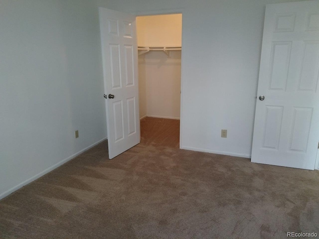 unfurnished bedroom with a walk in closet, a closet, and dark colored carpet