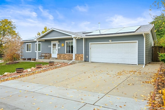 single story home with stone siding, concrete driveway, roof mounted solar panels, and an attached garage