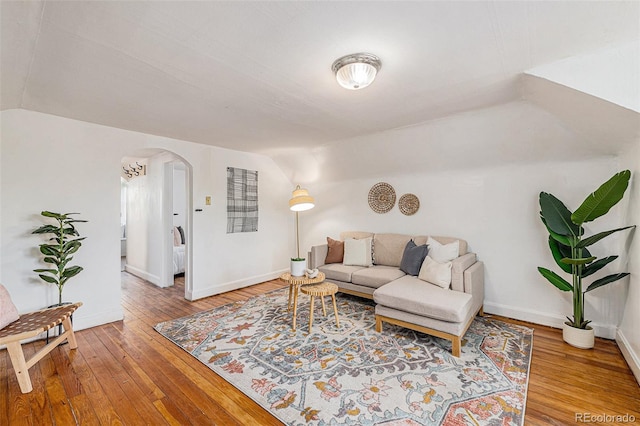 living room featuring arched walkways, baseboards, vaulted ceiling, and hardwood / wood-style flooring