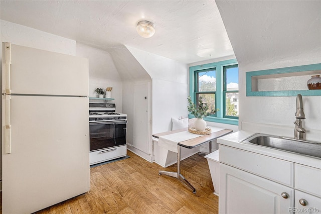 kitchen with white cabinets, a sink, white appliances, light countertops, and light wood-style flooring