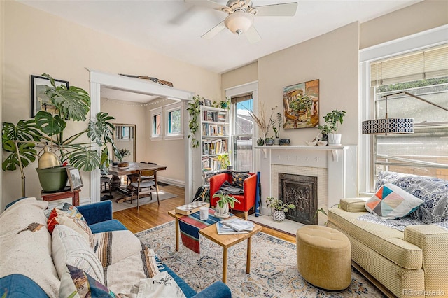 living area with ceiling fan, a brick fireplace, and wood finished floors