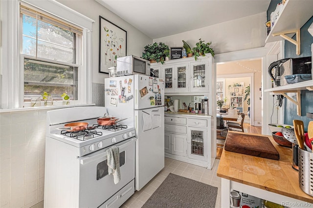 kitchen featuring white cabinetry, light tile patterned floors, white appliances, and glass insert cabinets