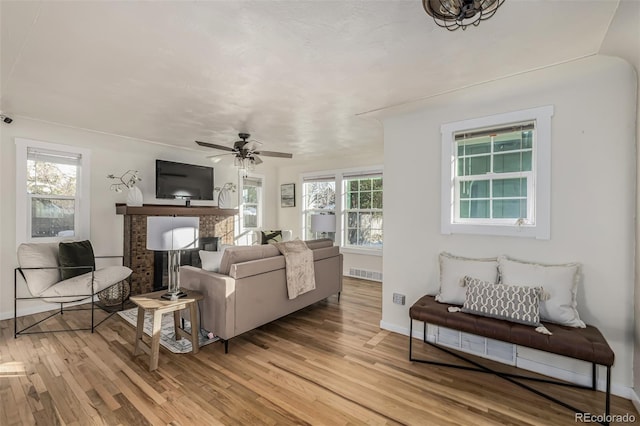 living room featuring light wood-type flooring, ceiling fan, a wealth of natural light, and a fireplace