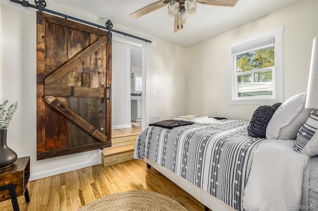 bedroom with ceiling fan, hardwood / wood-style floors, and a barn door