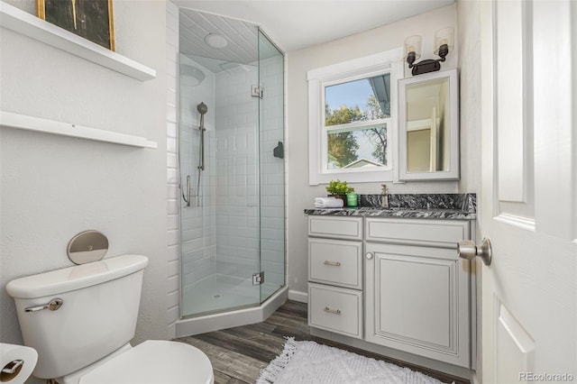 bathroom with hardwood / wood-style flooring, a shower with shower door, vanity, and toilet