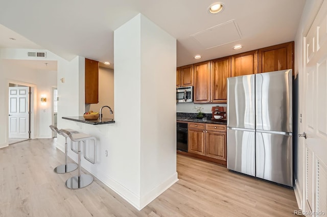 475 W 12th Ave Unit 9A, Denver, CO 80204 - kitchen featuring appliances with stainless steel finishes, brown cabinets, light wood-style flooring, recessed lighting, and a breakfast bar