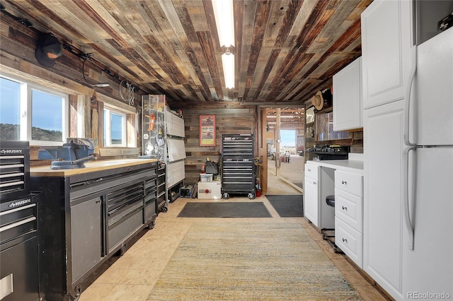 kitchen with light tile patterned floors, white refrigerator, wooden walls, white cabinets, and wood ceiling