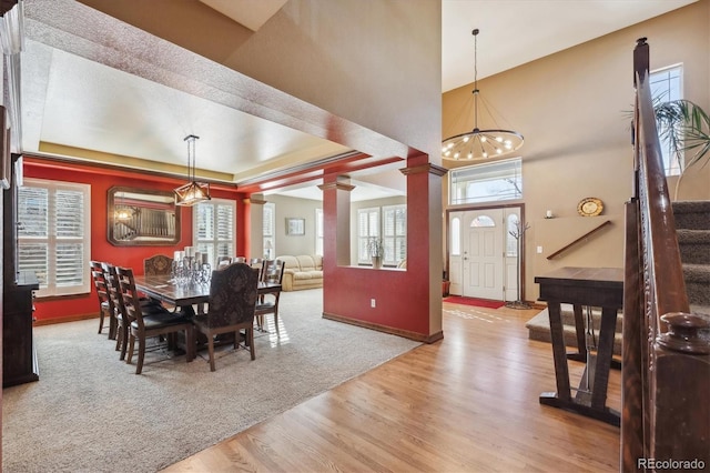 dining space featuring plenty of natural light, a tray ceiling, decorative columns, and wood finished floors