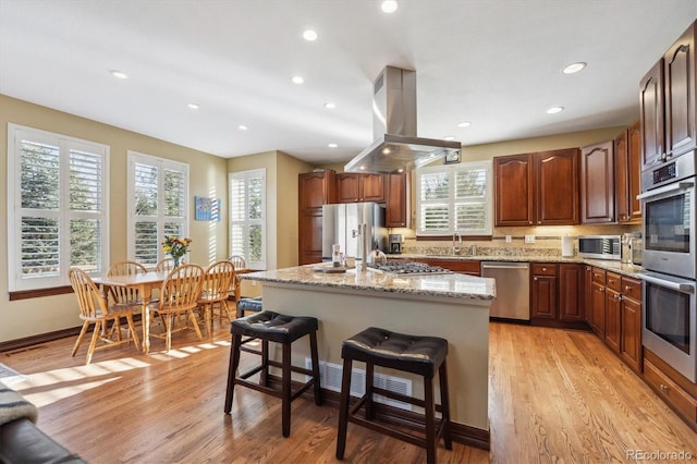 kitchen featuring light stone counters, stainless steel appliances, a breakfast bar, island exhaust hood, and a center island with sink