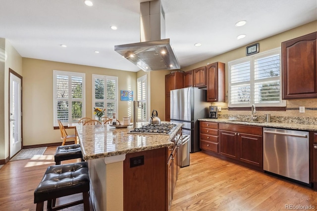 kitchen featuring stainless steel appliances, a breakfast bar, a sink, a center island, and island exhaust hood