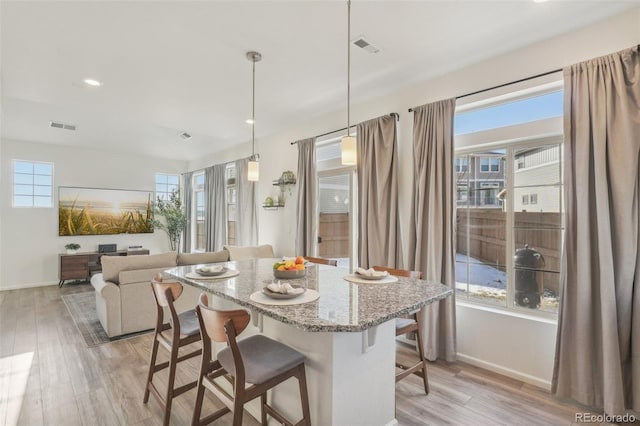 kitchen featuring a kitchen island, pendant lighting, a breakfast bar area, light stone counters, and light wood-type flooring