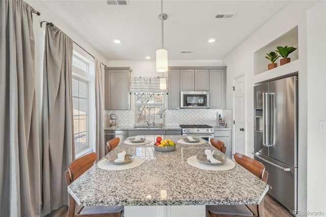 kitchen featuring sink, gray cabinetry, high quality appliances, a kitchen island, and pendant lighting