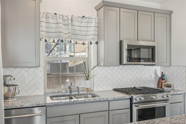 kitchen featuring appliances with stainless steel finishes, light stone countertops, sink, and gray cabinetry