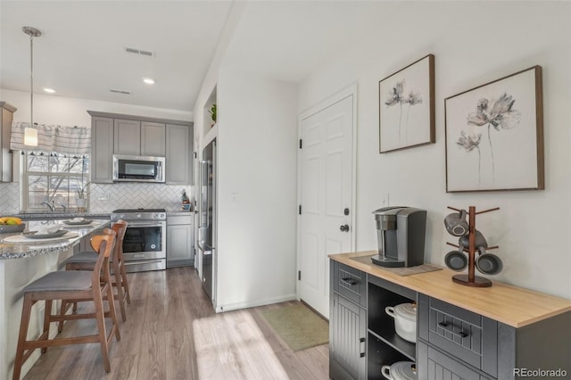 kitchen with appliances with stainless steel finishes, gray cabinetry, hanging light fixtures, backsplash, and light wood-type flooring