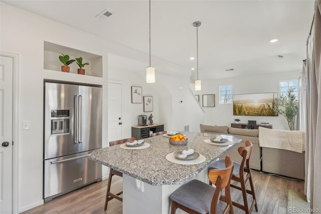 kitchen with pendant lighting, high quality fridge, a breakfast bar, and light hardwood / wood-style floors