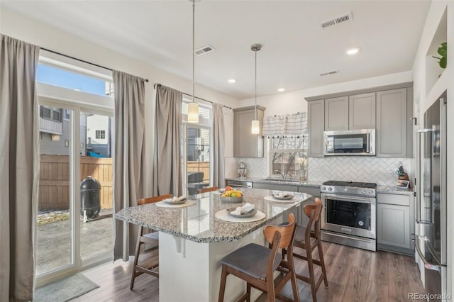 kitchen featuring a kitchen island, decorative light fixtures, a breakfast bar area, light stone counters, and stainless steel appliances