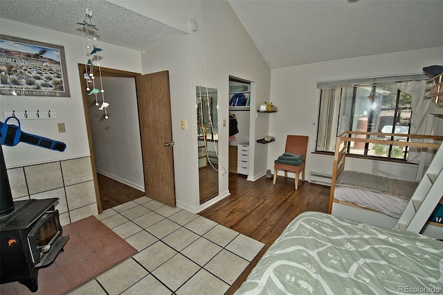 interior space with baseboard heating, a textured ceiling, lofted ceiling, a wood stove, and a closet