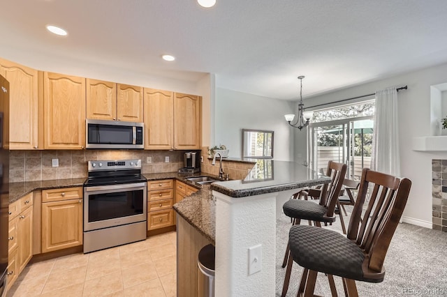 kitchen with stainless steel appliances, light brown cabinetry, and a sink