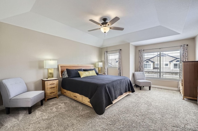 bedroom with a raised ceiling, baseboards, light colored carpet, and ceiling fan