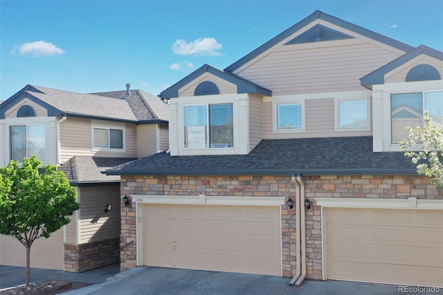 townhome / multi-family property featuring stone siding, aphalt driveway, roof with shingles, and a garage