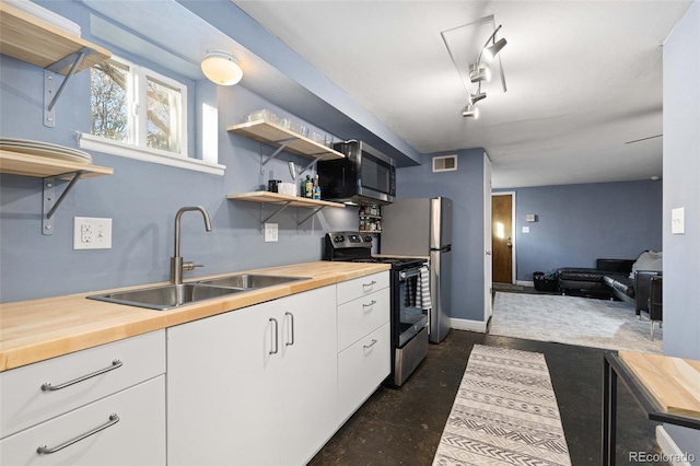 kitchen with butcher block countertops, stainless steel appliances, a sink, and open shelves