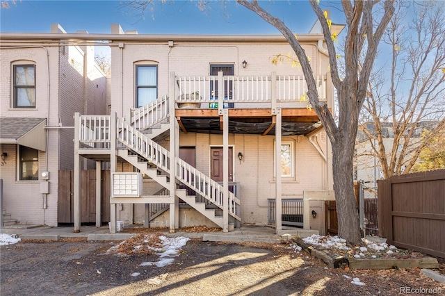 back of property featuring stairway, a wooden deck, brick siding, and fence
