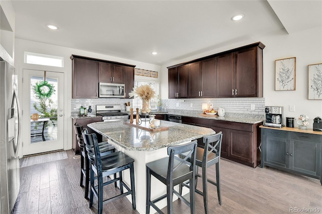 240 S Oak Hill St, Aurora, CO 80018 - kitchen with appliances with stainless steel finishes, a kitchen bar, dark brown cabinetry, backsplash, and recessed lighting