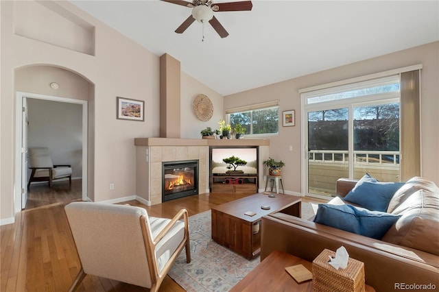 living area with lofted ceiling, light wood-type flooring, baseboards, and a tiled fireplace