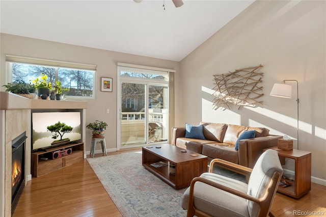 interior space with lofted ceiling, light wood-style floors, a glass covered fireplace, a ceiling fan, and baseboards