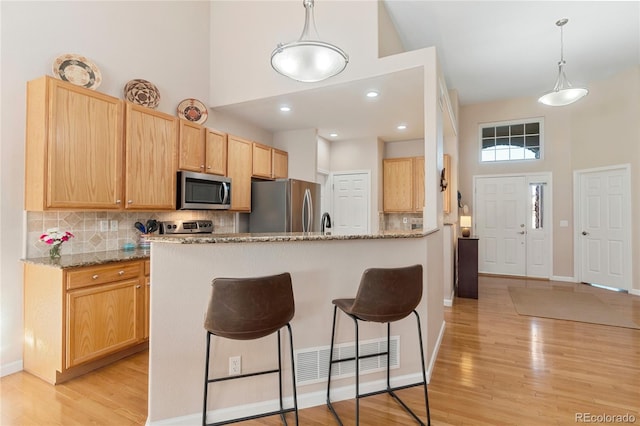 kitchen with visible vents, a towering ceiling, appliances with stainless steel finishes, light stone counters, and hanging light fixtures