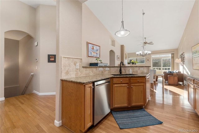 kitchen featuring arched walkways, brown cabinets, light stone countertops, stainless steel dishwasher, and a sink