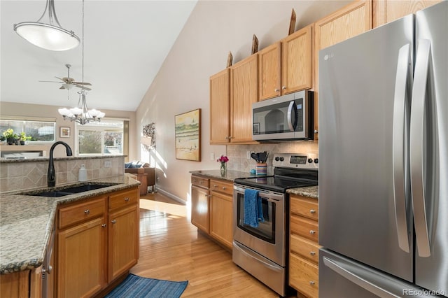 kitchen featuring lofted ceiling, stainless steel appliances, light wood-style floors, pendant lighting, and a sink