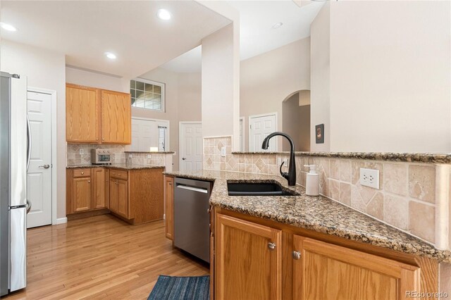 kitchen featuring light stone counters, a peninsula, a sink, appliances with stainless steel finishes, and light wood-type flooring