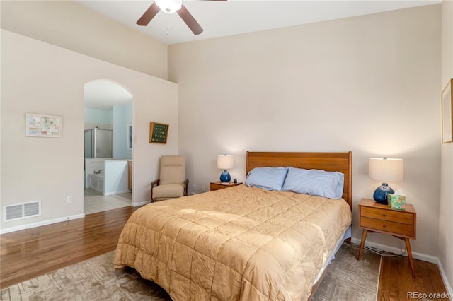 bedroom featuring arched walkways, visible vents, ensuite bathroom, wood finished floors, and baseboards