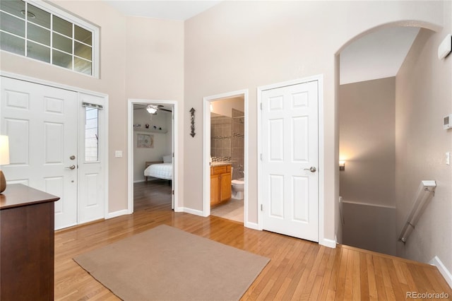 entrance foyer with light wood-style flooring, a high ceiling, arched walkways, and baseboards