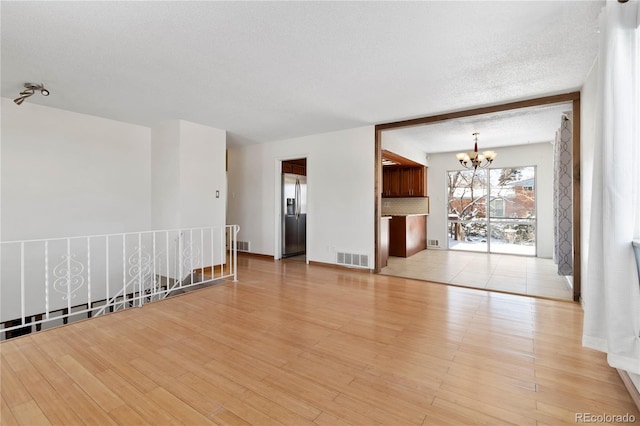 empty room with beam ceiling, an inviting chandelier, light hardwood / wood-style floors, and a textured ceiling
