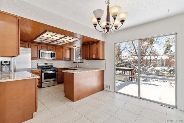 kitchen with kitchen peninsula, pendant lighting, appliances with stainless steel finishes, sink, and decorative backsplash