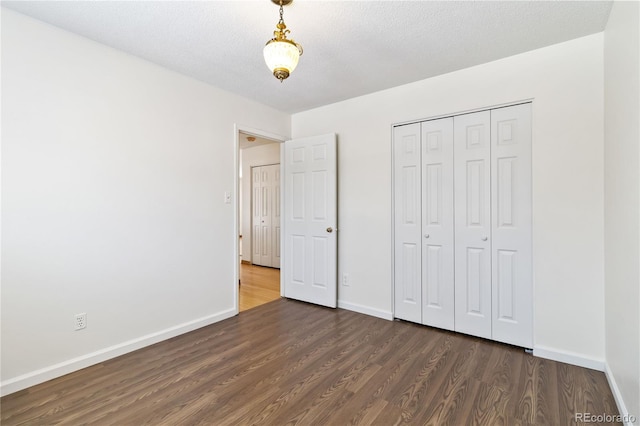 unfurnished bedroom with a closet, a textured ceiling, and dark hardwood / wood-style floors