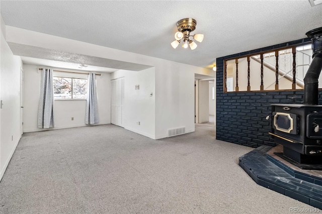 unfurnished living room with light carpet, a textured ceiling, and a wood stove