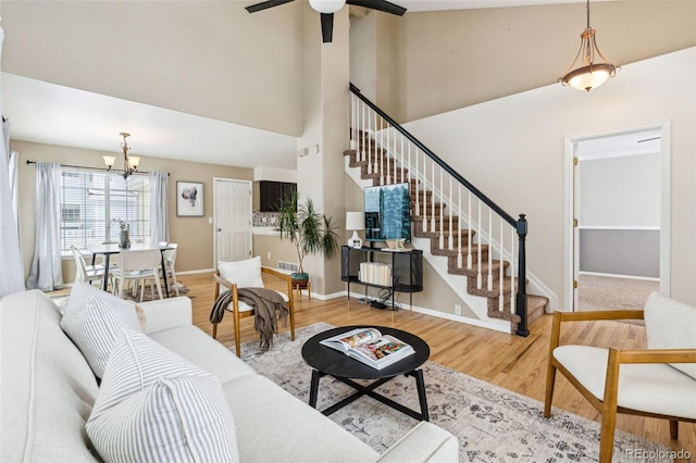 living room with high vaulted ceiling, ceiling fan with notable chandelier, and light hardwood / wood-style floors