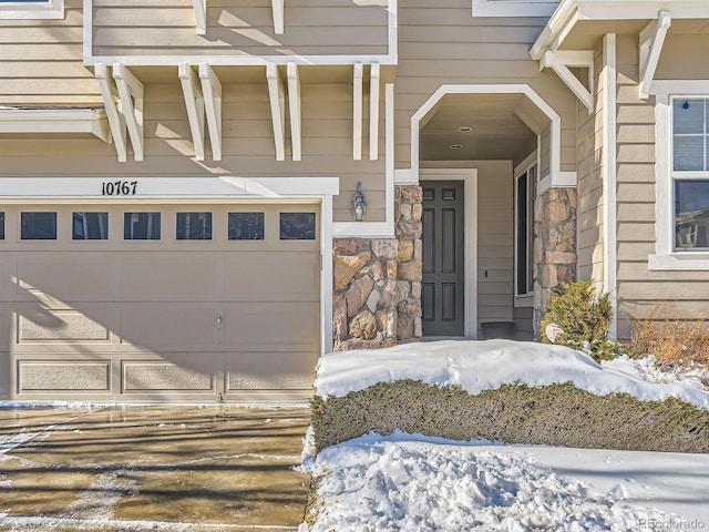 snow covered property entrance featuring a garage