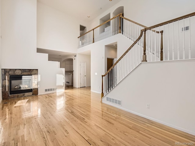 unfurnished living room featuring a towering ceiling, a fireplace, and light wood-type flooring