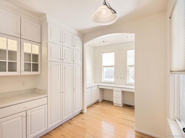 kitchen with pendant lighting, built in desk, light hardwood / wood-style floors, and white cabinetry