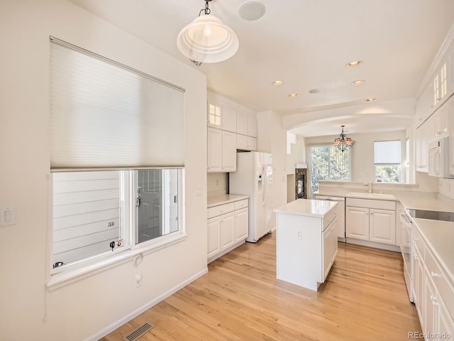 kitchen with decorative light fixtures, white appliances, a center island, and white cabinetry