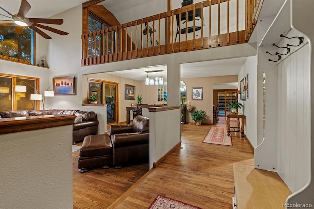 living area with ceiling fan with notable chandelier, a high ceiling, and wood finished floors