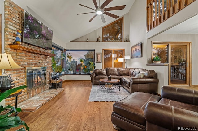 living area with high vaulted ceiling, a ceiling fan, wood finished floors, baseboards, and a brick fireplace