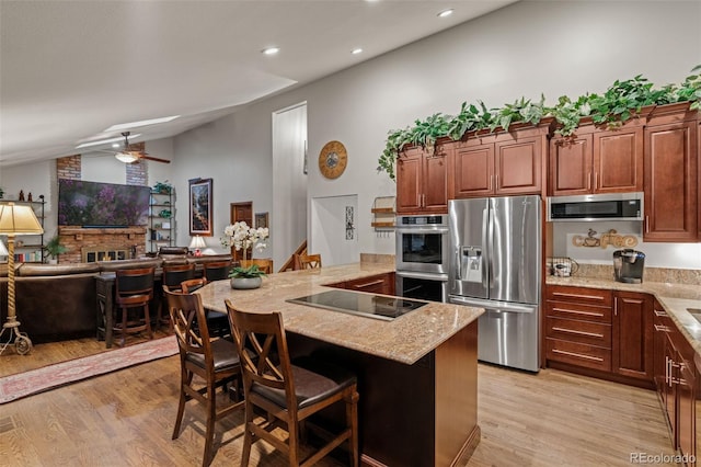 kitchen featuring light stone counters, a breakfast bar, vaulted ceiling, light wood-style floors, and appliances with stainless steel finishes