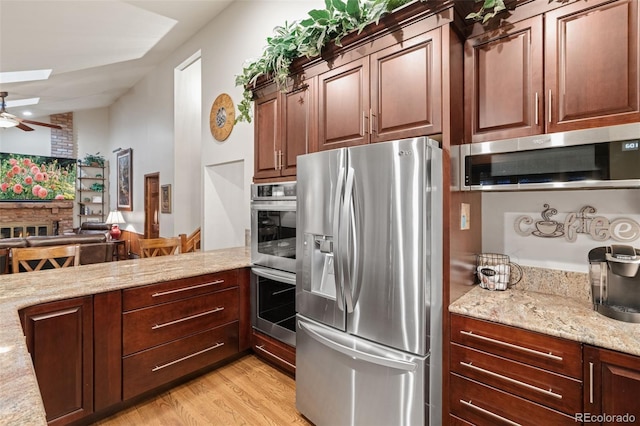 kitchen with light stone counters, a ceiling fan, a skylight, light wood-style floors, and appliances with stainless steel finishes