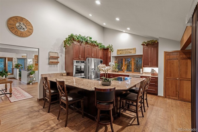 kitchen with light wood-type flooring, light stone counters, stainless steel appliances, a peninsula, and a breakfast bar area